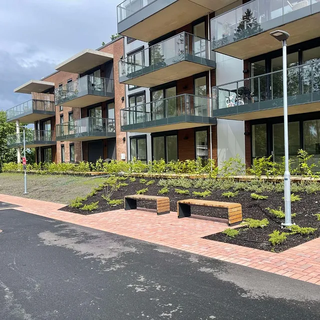 Nymoderne leilighetsbygg med balkonger og nyanlagt uteområde med beplantning og benker.