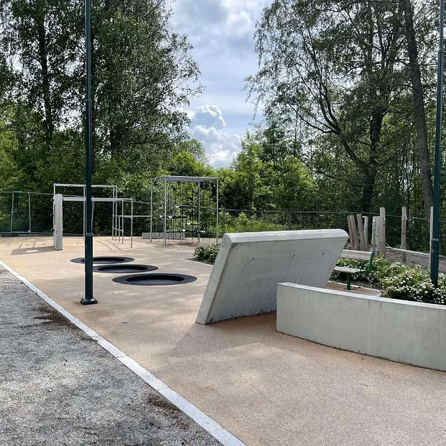 Moderne utendørs treningspark med betonghindre, metallstenger og trampolinefelt i bakken.