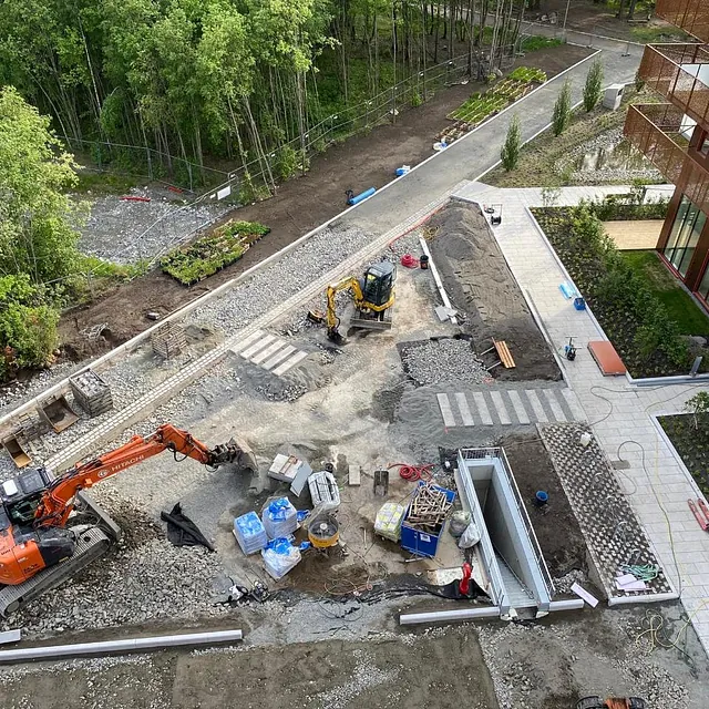 Utsikt over byggeplass med gravemaskiner, gangfelt, plantekasser og belegningsstein.
